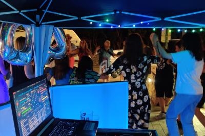 Des personnes dansent sous un chapiteau éclairé, avec une table de mixage et un ordinateur au premier plan.