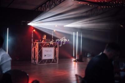 Un DJ mixe sur une scène éclairée par des projecteurs et des lumières colorées dans une salle sombre.