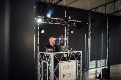 Un DJ mixe sur une scène équipée de lumières et d'un équipement audio dans une salle aux rideaux sombres.