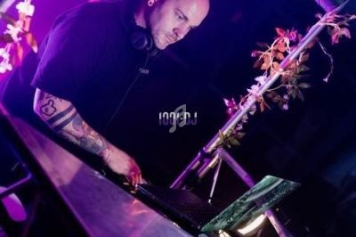 Un DJ mixe de la musique sur une table équipée d'un ordinateur portable, entouré de décorations végétales.