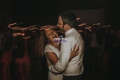 Un couple danse tendrement lors d'une fête, entouré de lumières floues et d'invités en arrière-plan.