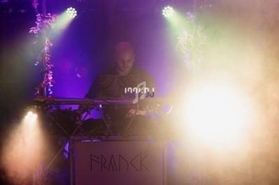 Un DJ mixe sur une scène éclairée par des lumières colorées et entourée de décorations végétales.