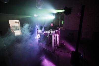 Un DJ mixe sur une scène éclairée par des projecteurs colorés et entourée de fumée dans une ambiance nocturne.