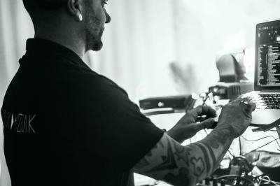 Un DJ mixe de la musique sur une table de mixage, concentré sur son ordinateur portable dans une ambiance lumineuse.