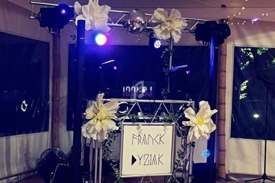 Structure de DJ décorée de fleurs blanches et éclairée par des lumières colorées dans une salle couverte.