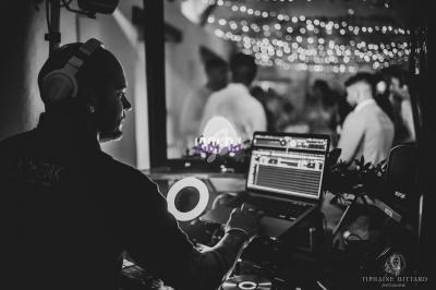 Un DJ mixe de la musique sur son équipement dans une ambiance festive avec des lumières tamisées en arrière-plan.