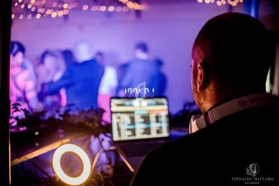 Un DJ mixe de la musique sur un ordinateur portable lors d'une soirée avec des lumières tamisées et des invités dansant.