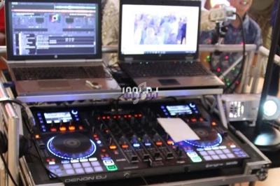 Poste de DJ avec une table de mixage, deux ordinateurs portables affichant des logiciels et un projecteur à proximité.