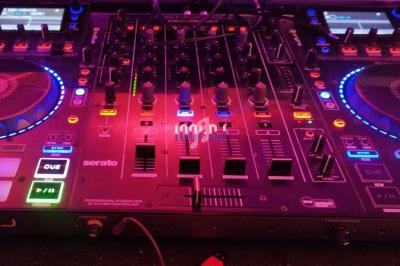 Table de mixage DJ avec platines, boutons et curseurs éclairés par des lumières colorées dans un environnement sombre.