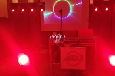 Équipement de DJ avec éclairage rouge, écran projetant un visuel lumineux et logo ADJ visible sur la structure.