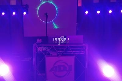 Installation de matériel de sonorisation et d'éclairage avec projecteurs violets et écran affichant un visuel lumineux.