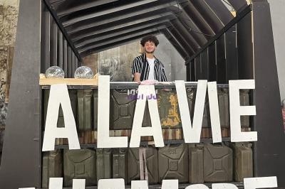Stand décoré avec des lettres géantes ’À la vie, à l’amore’, animé par une personne sous une structure en bois.