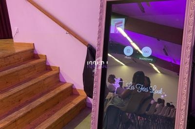 Miroir interactif avec cadre décoratif, affichant des options photo et boomerang, placé près d'un escalier en bois.