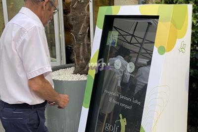 Un homme interagit avec une borne tactile d'information sur un parcours de golf, installée en extérieur.