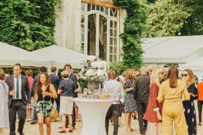 Groupe de personnes discutant dans une cour gravillonnée devant un bâtiment ancien entouré de verdure.