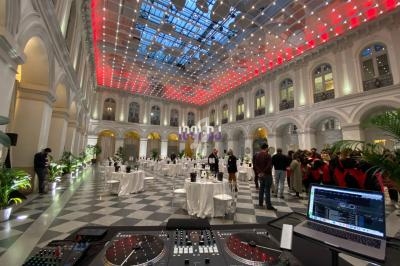 Salle élégante avec verrière illuminée, tables dressées pour un événement, vue depuis une table de mixage DJ.
