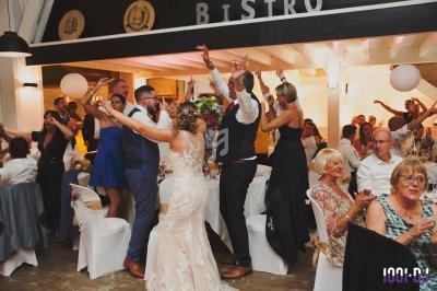 Des invités dansent et célèbrent dans une salle de réception décorée, avec des tables dressées et une ambiance festive.