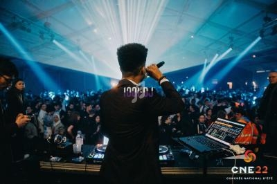 Un DJ anime une soirée dans une grande salle remplie de spectateurs sous des jeux de lumière.