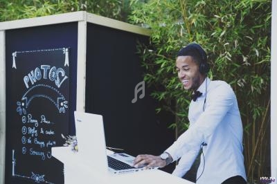 Un homme souriant, portant un casque audio, utilise un ordinateur portable devant un panneau ’Photobooth’.