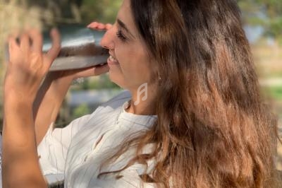 Femme secouant un shaker en métal dans un cadre extérieur ensoleillé avec des arbres en arrière-plan.