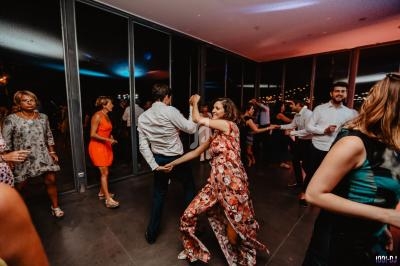 Des personnes dansent dans une salle vitrée éclairée, lors d'un événement festif en soirée.