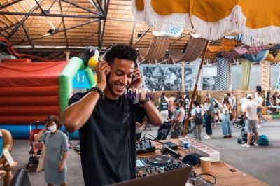 Un DJ mixe de la musique sur une table de mixage dans un espace intérieur animé avec des visiteurs en arrière-plan.