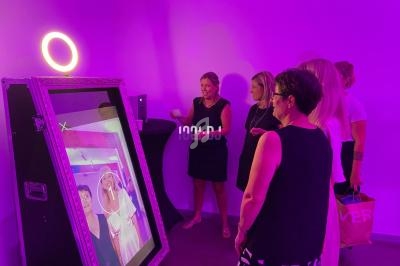 Des personnes interagissent avec un miroir photo interactif dans une pièce éclairée par une lumière violette.