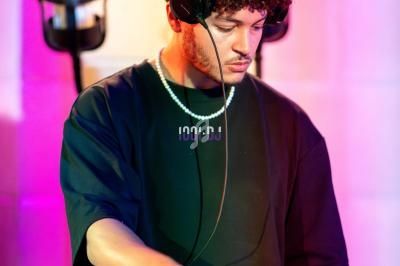 Un DJ portant un casque audio mixe de la musique sur une table de mixage dans une ambiance lumineuse colorée.