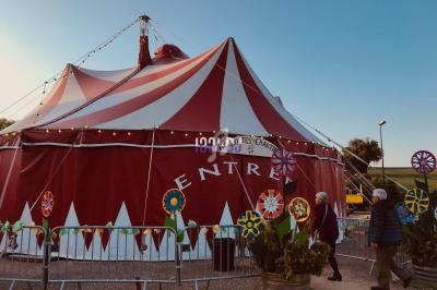Chapiteau de cirque rouge et blanc avec des décorations florales colorées, entouré de barrières, au crépuscule.