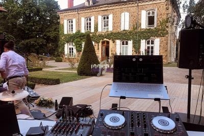 Vue d'une console de mixage et d'un ordinateur portable installés en extérieur devant une grande maison en pierre.