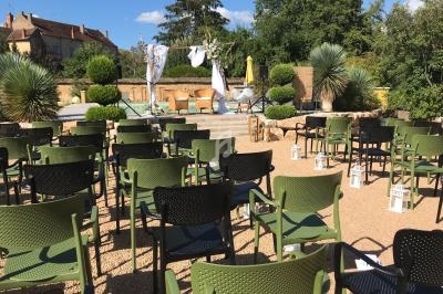 Chaises disposées en rangées face à une petite scène extérieure décorée, entourée de végétation et de bâtiments en arrière…