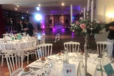 Salle de réception décorée avec des tables dressées, chandelier fleuri et éclairage d'ambiance violet en arrière-plan.