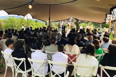 Cérémonie en plein air sous une tente, avec des invités assis sur des chaises blanches et un couple au centre.