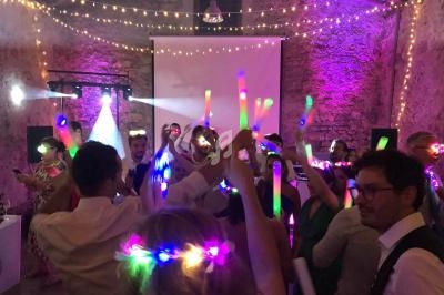 Groupe de personnes dansant sous des guirlandes lumineuses, tenant des bâtons lumineux dans une ambiance festive.