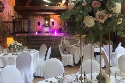Salle de réception décorée avec des tables rondes, nappes blanches, et un grand bouquet floral au premier plan.
