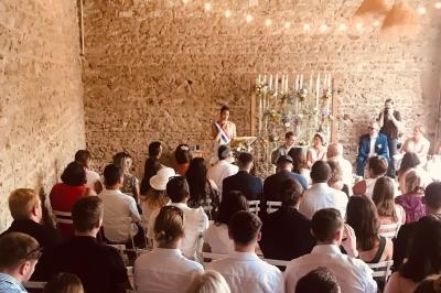 Une cérémonie civile se déroulant dans une salle en pierre avec des invités assis et une officière en écharpe tricolore.