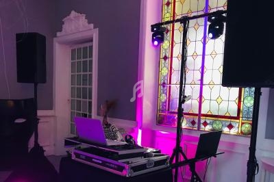 Installation de matériel de DJ avec enceintes et éclairages colorés dans une salle avec vitrail et décor élégant.