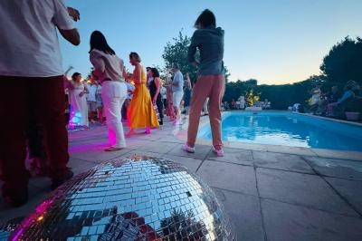Groupe de personnes dansant près d'une piscine au crépuscule, avec une boule à facettes au premier plan.