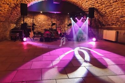 Scène de concert dans une cave voûtée en pierre, éclairée par des projecteurs roses et violets.