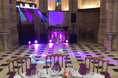 Salle de réception dans une église rénovée, avec tables dressées et éclairage coloré près d'un autel.