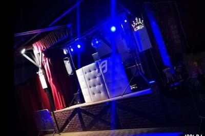 Scène éclairée en bleu avec une cabine de DJ, des rideaux rouges et des équipements audio.