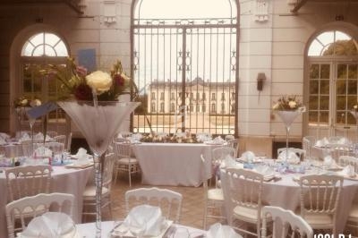 Salle de réception élégante avec tables décorées de fleurs, vue sur un bâtiment historique à travers une grille ouverte.