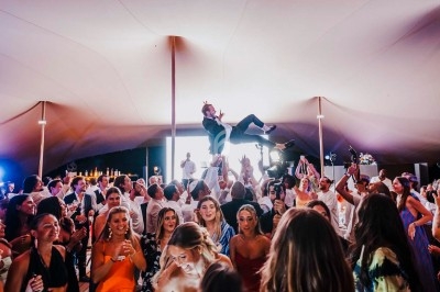 Groupe de personnes dansant sous une tente, avec un homme porté en l'air par la foule au centre de la scène.
