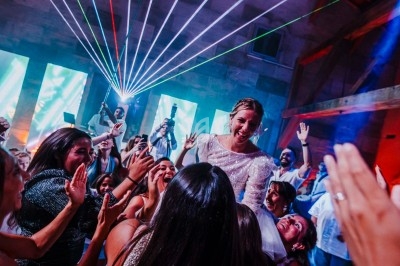 Une mariée souriante entourée d'invités dansant sous des lumières colorées et des lasers lors d'une fête.