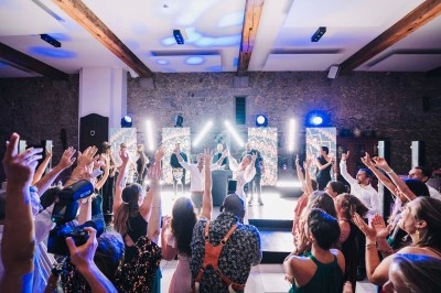 Groupe de personnes dansant et levant les bras lors d'une fête animée avec éclairages colorés et musique en direct.