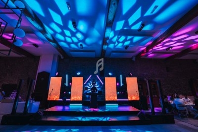 Salle de réception avec éclairage coloré, scène équipée de panneaux lumineux et tables dressées en arrière-plan.