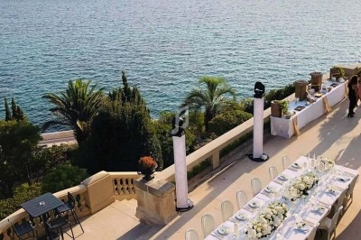 Grande table décorée de fleurs blanches sur une terrasse surplombant la mer, entourée de végétation méditerranéenne.
