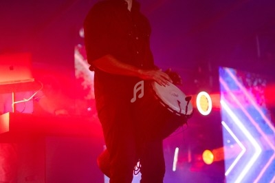 Un musicien joue du tambour sous des lumières colorées dans une ambiance de scène.
