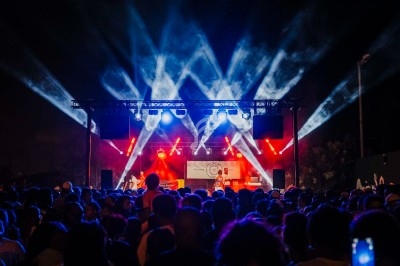 Foule rassemblée devant une scène illuminée par des projecteurs colorés lors d'un concert en plein air nocturne.