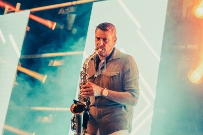 Un musicien joue du saxophone sur scène, entouré de lumières colorées et d'écrans lumineux.